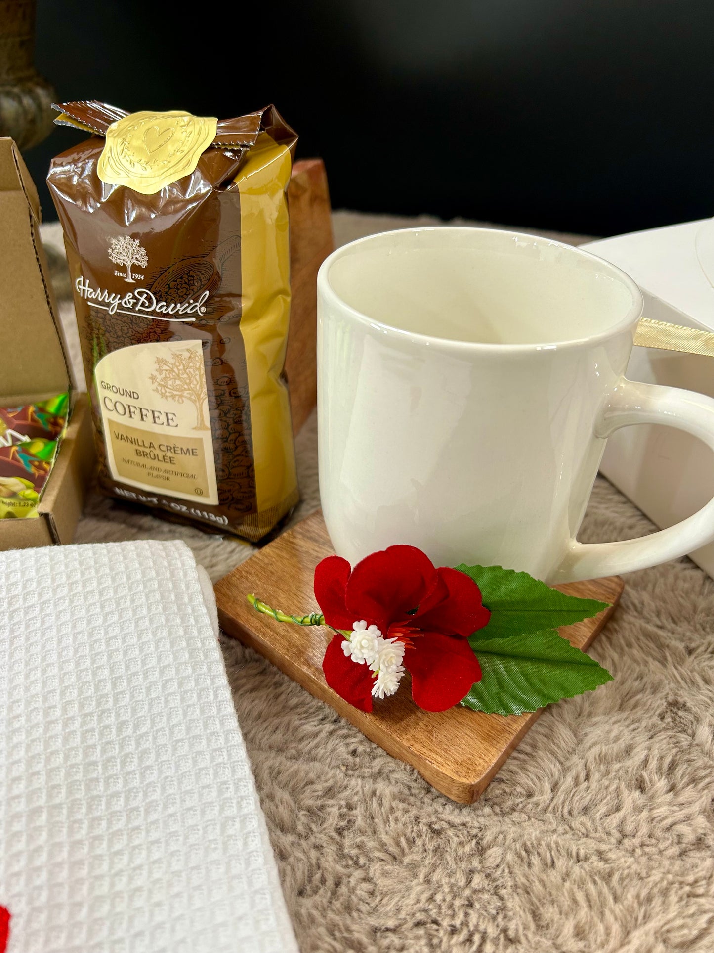 White mug with a red flower on a wooden coaster next to a bag of Harry & David coffee.