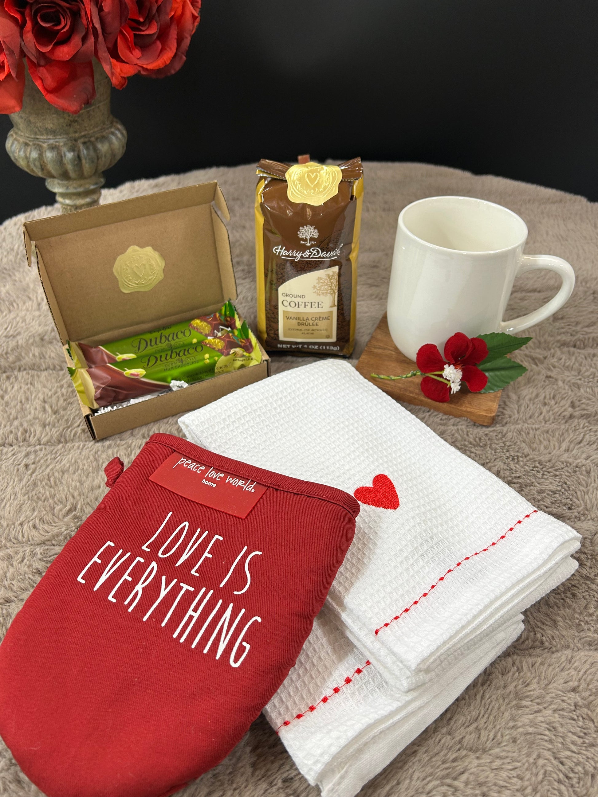 Red oven mitt with 'Love is Everything' text, white mug, and kitchen items on a textured surface.