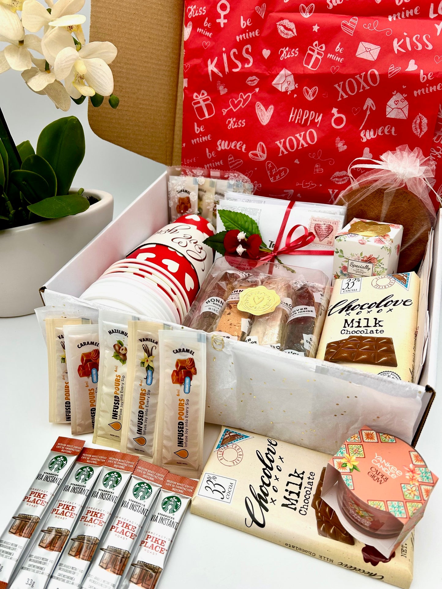 Gourmet valentines gift box with coffee syrup, biscotti, coffee, and chocolate on a white surface.