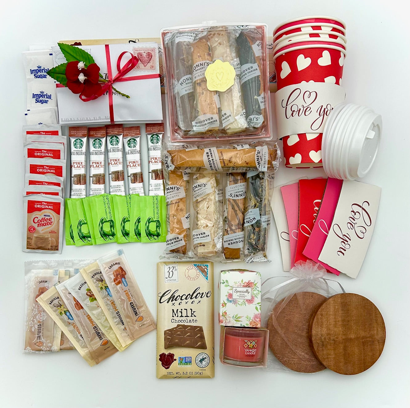 Collection of coffee and accessories including Starbucks Via packets, sugar packets, coffee cups, biscotti, candle, heart envelopes bundle, and wooden coaster on a white background.